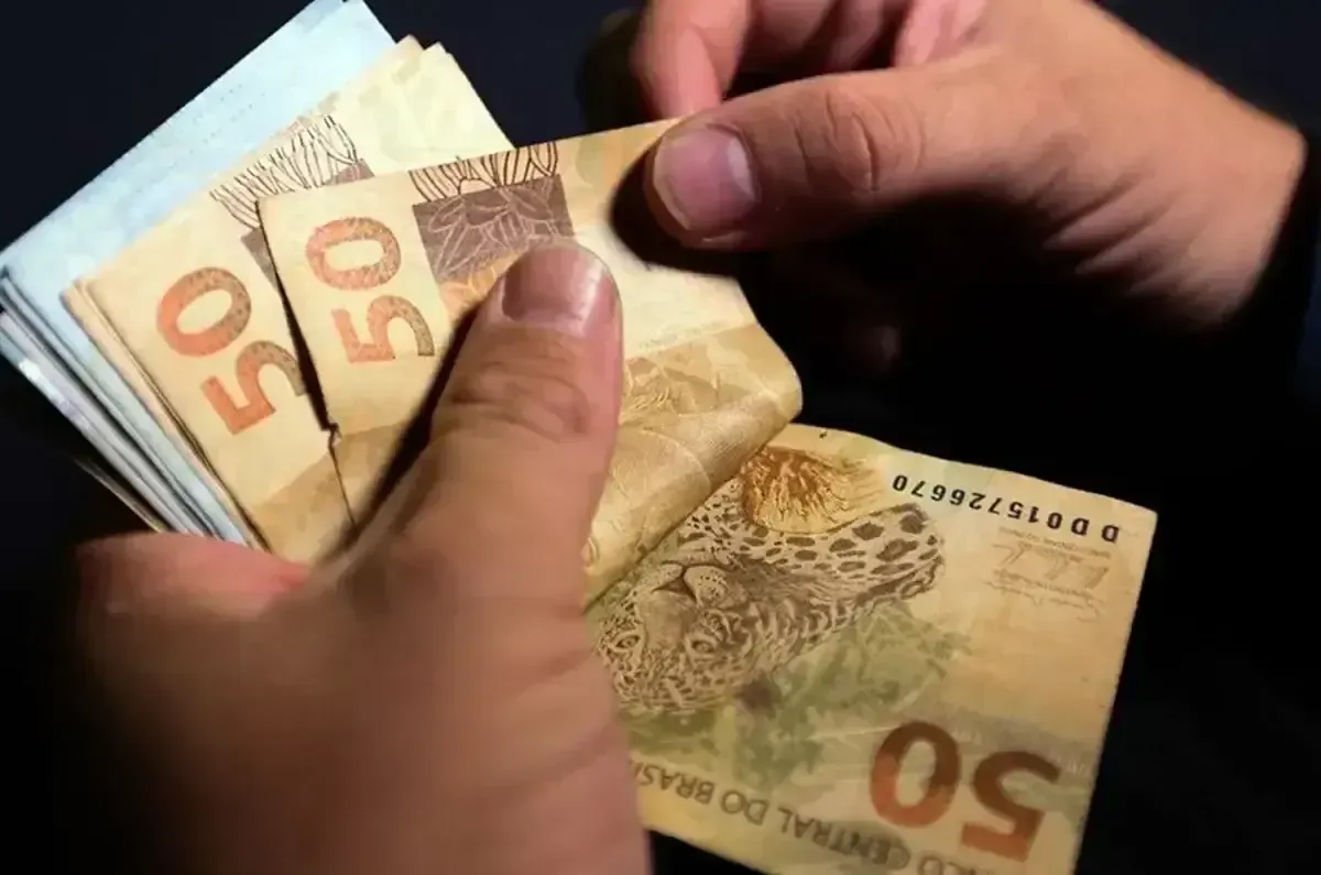 Pessoas contando notas de R$ 50, simbolizando o pagamento dos salários.