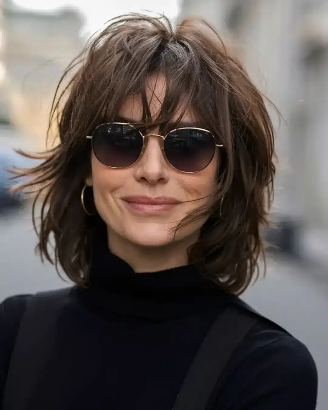 Mulher com corte shag haircut em cabelo castanho médio com franja desfiada.