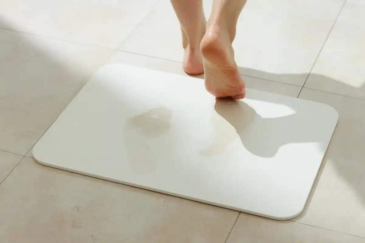 Pés molhados sobre tapete antiderrapante em piso de banheiro.
