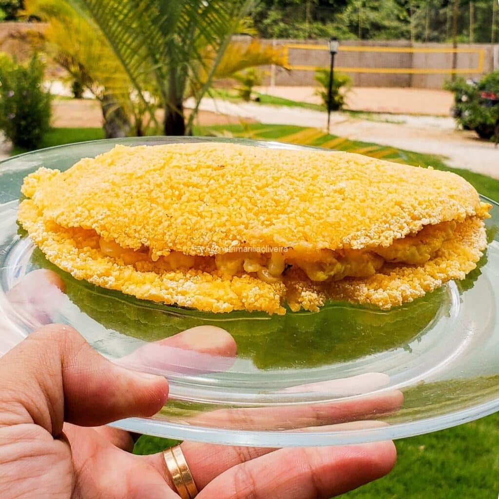 Tapioca de cuscuz dourada no prato de vidro sendo segurada ao ar livre