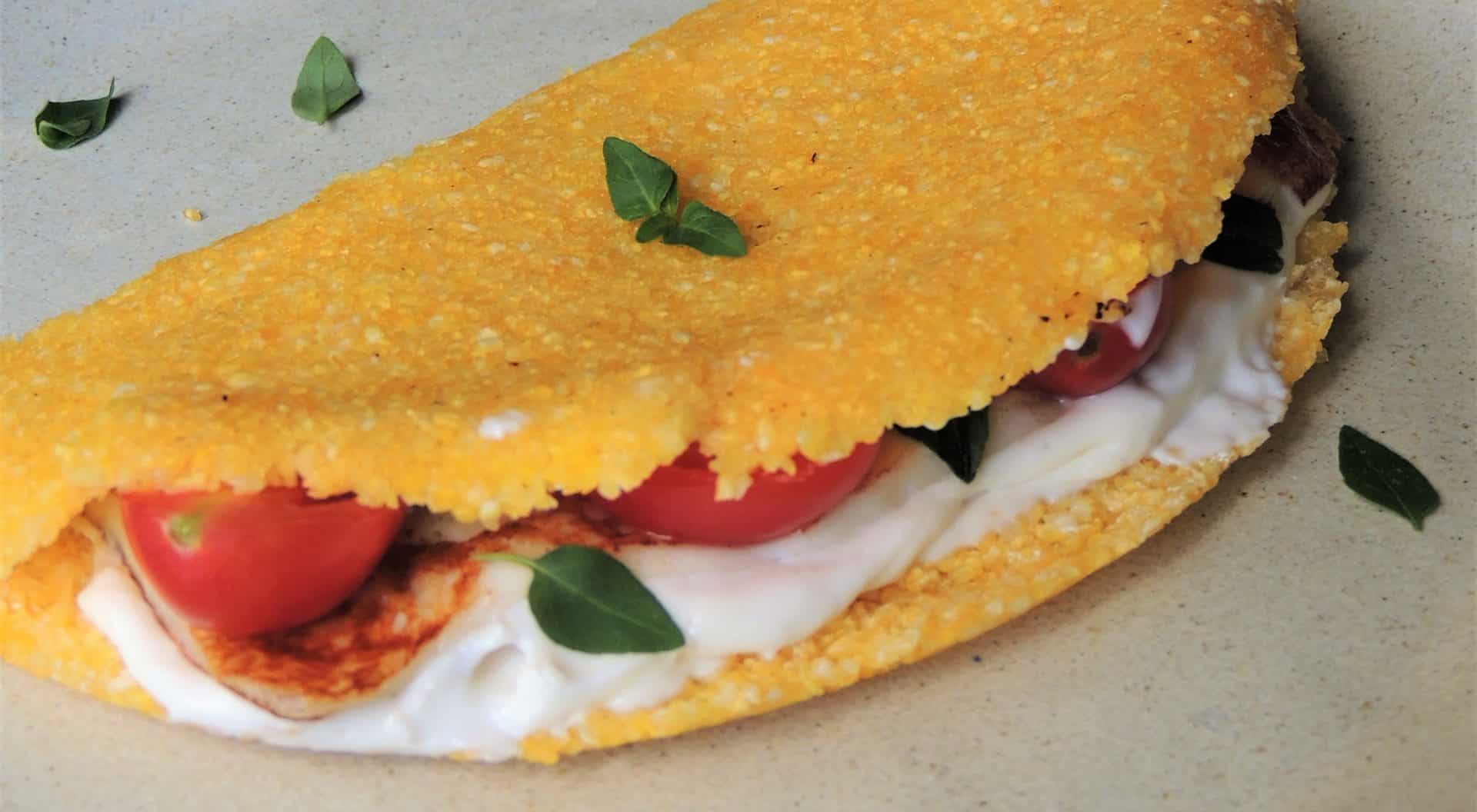 Tapioca de cuscuz recheada com frango, tomate, queijo cremoso e folhas de manjericão