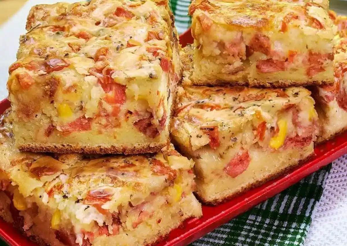 Fatias de torta salgada com queijo derretido, tomate, milho e uma crosta dourada sobre um prato vermelho.