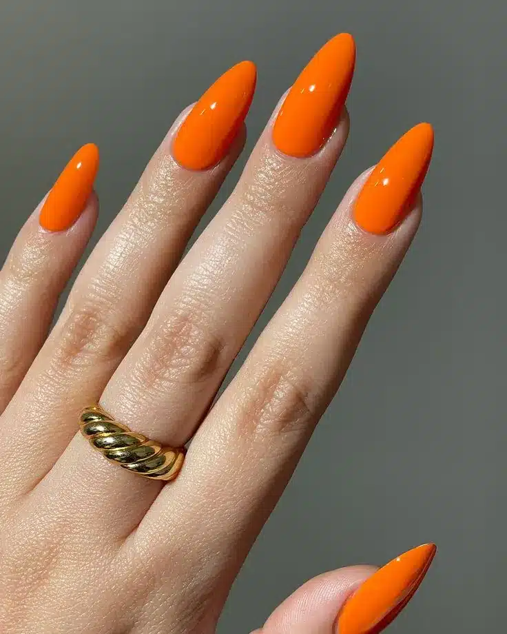 Unhas com esmalte laranja tangerina em formato stiletto e anel dourado