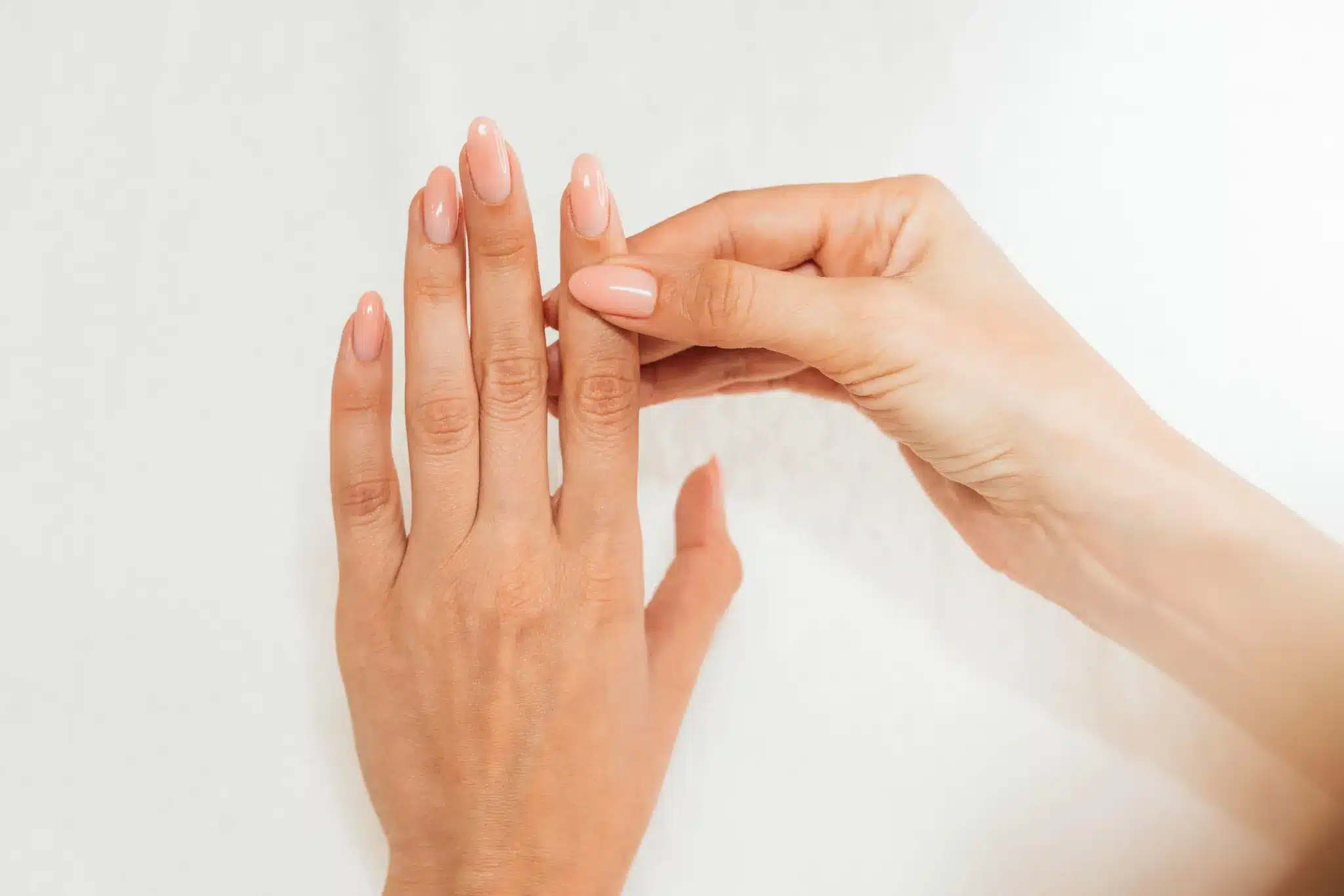 Mãos femininas cuidadas com unhas longas e esmalte nude em fundo branco