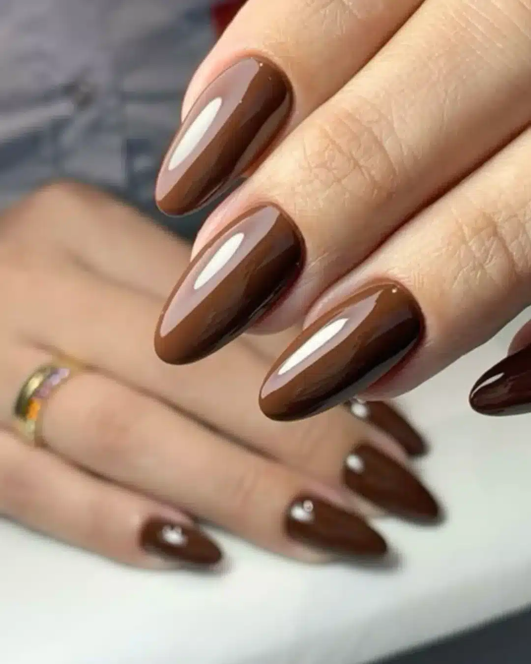 Unhas longas em formato amendoado com esmalte marrom chocolate e brilho intenso.