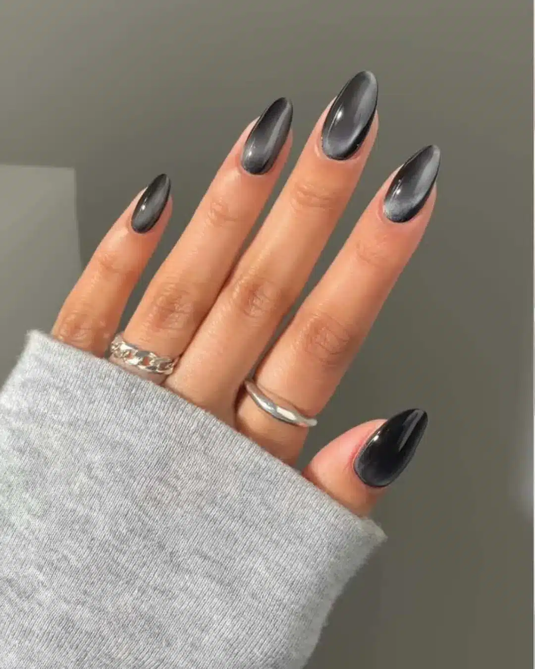 Unhas longas no formato amendoado com esmalte preto fumê e acabamento brilhante.