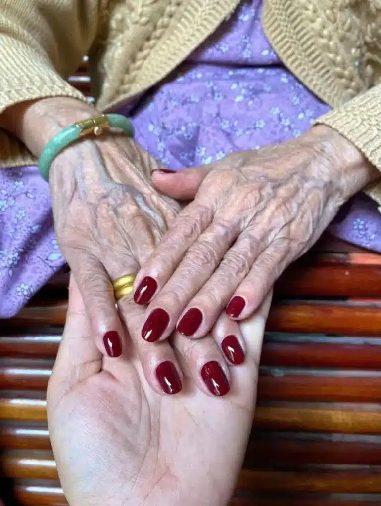 Unhas com esmalte vermelho intenso em mãos de mulher idosa