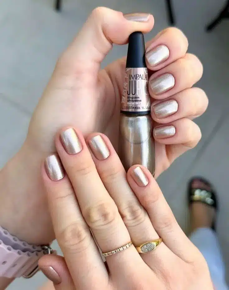 Unhas curtas e bem cuidadas com esmalte metálico em tom dourado, representando a escolha sofisticada das mulheres ricas.
