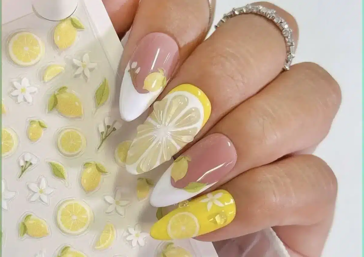 Unhas de porcelana decoradas com desenhos de limões e flores, com detalhes em tons de amarelo e branco.