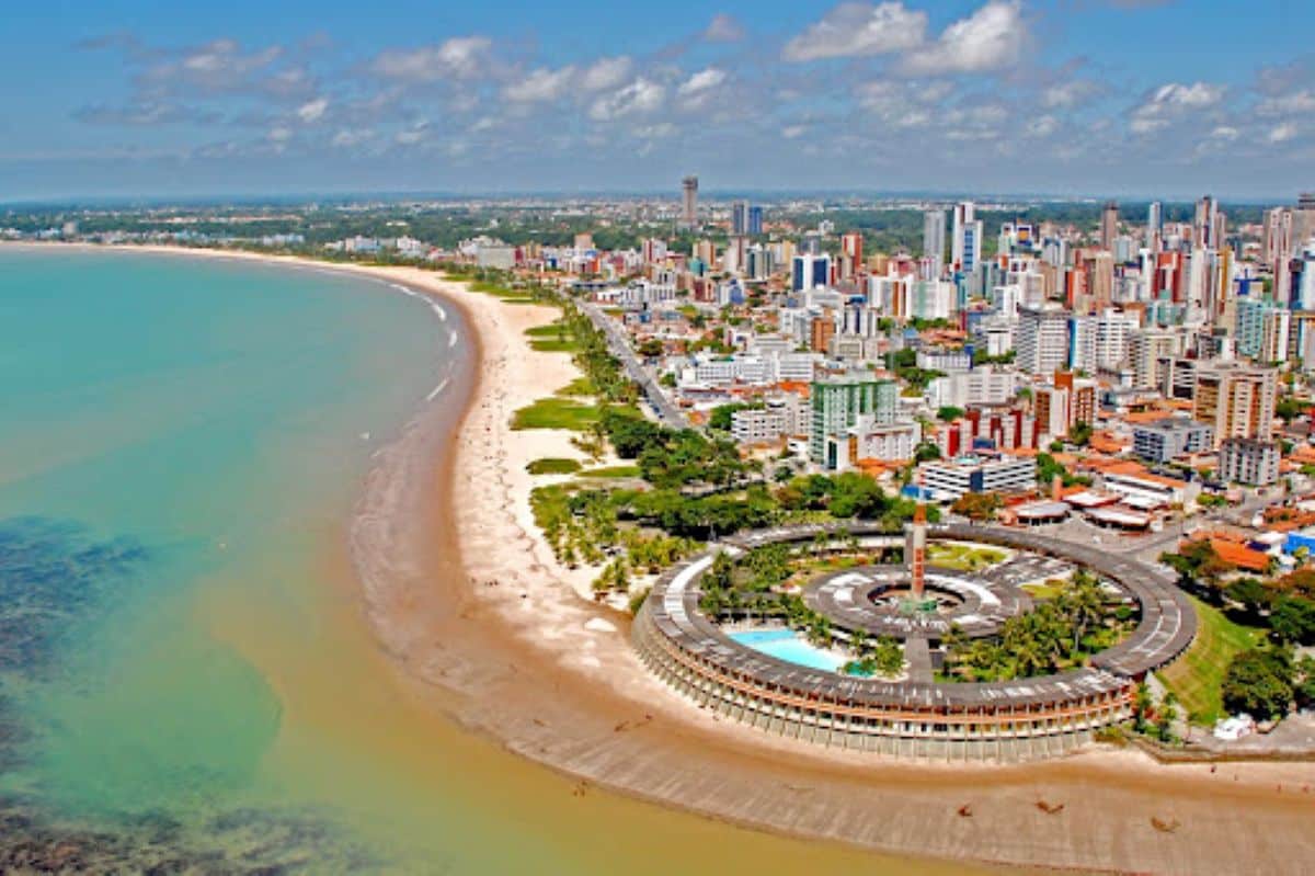Vista aérea de cidade litorânea no Nordeste com orla urbanizada e prédios modernos.