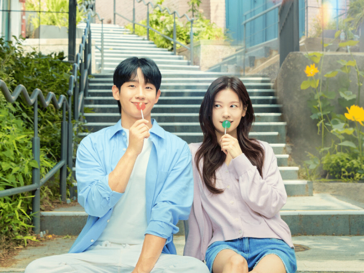 Casal sorridente, um homem e uma mulher jovens asiáticos, sentados em uma escadaria externa, ambos segurando pirulitos.