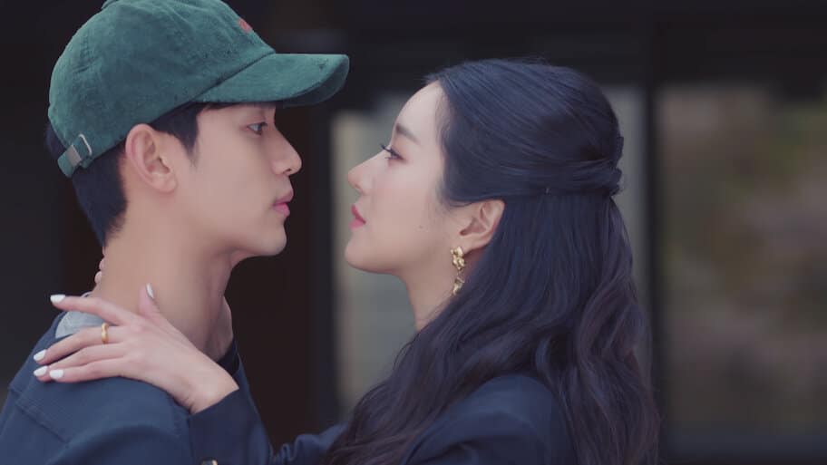 Cena de "Tudo Bem Não Ser Normal" onde Ko Moon-young, a escritora, segura o rosto de Moon Gang-tae, o cuidador, em um momento de intensa conexão visual. A imagem mostra a química inegável entre os personagens.