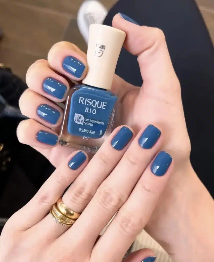 Unhas pintadas com esmalte azul profundo cremoso, mostrando uma manicure elegante com esmalte da marca Risqué.