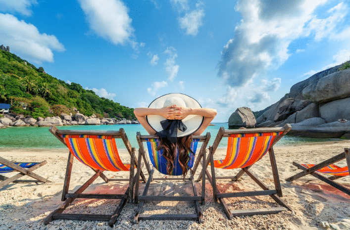 Mulher relaxando em cadeira de praia colorida diante de mar cristalino, representando destinos ideais para feriados prolongados em setembro.
