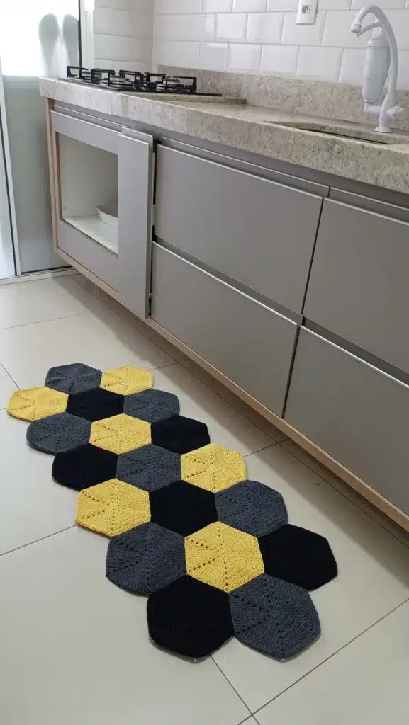 Tapete de crochê 3D em formato hexagonal nas cores amarelo, cinza e preto, em ambiente moderno com móveis de estilo industrial.