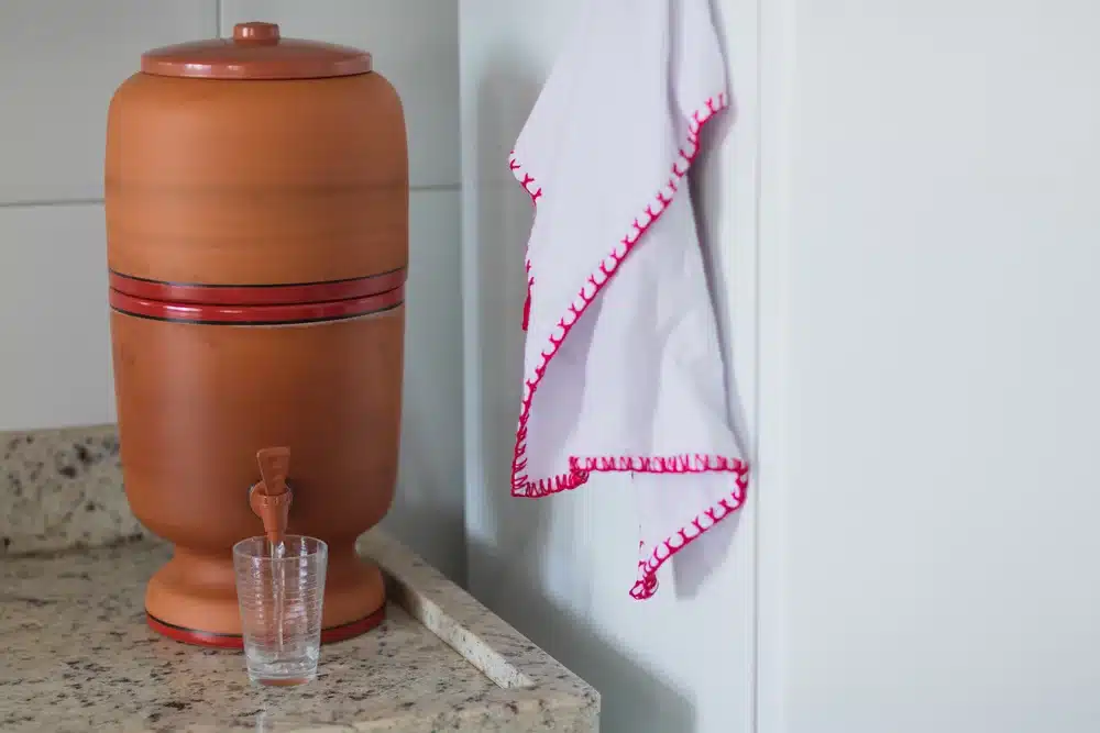 Filtro de barro sobre a bancada da cozinha, com um copo de água ao lado.