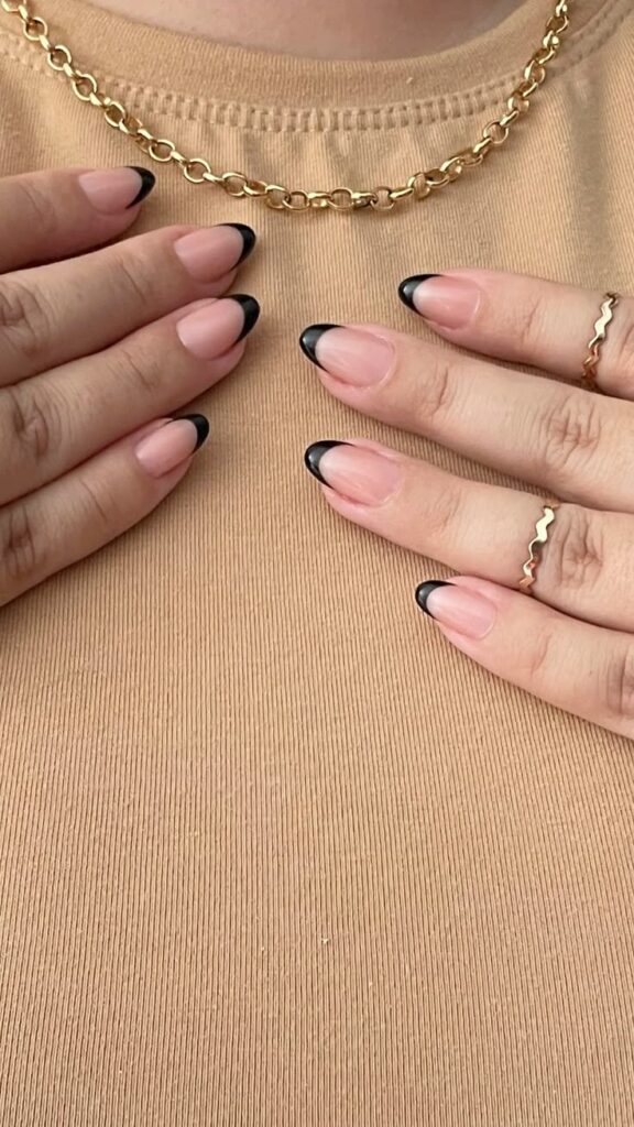 Mãos com unhas em formato oval, apresentando uma francesinha preta minimalista e elegante.