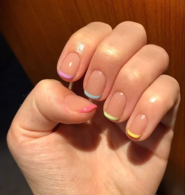 Unhas com francesinha colorida em tons vibrantes de rosa, azul, verde e amarelo sobre base nude