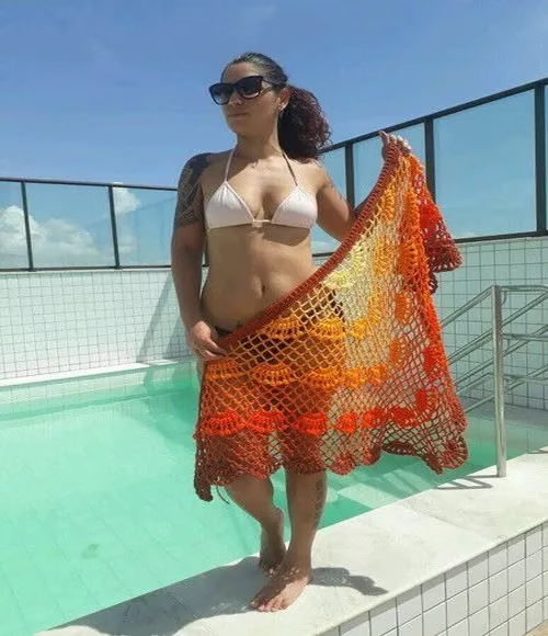 Mulher de biquíni segurando saída de praia de crochê laranja com detalhes em degradê