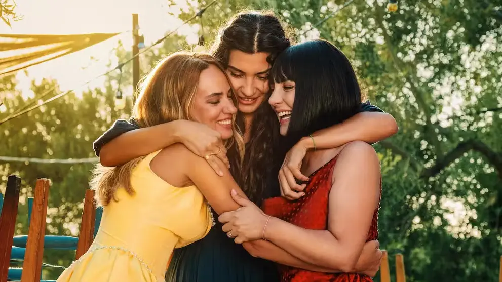 Três amigas sorridentes, Tuba Büyüküstün, Seda Bakan e Boncuk Yılmaz, se abraçam na série Uma Nova Mulher.