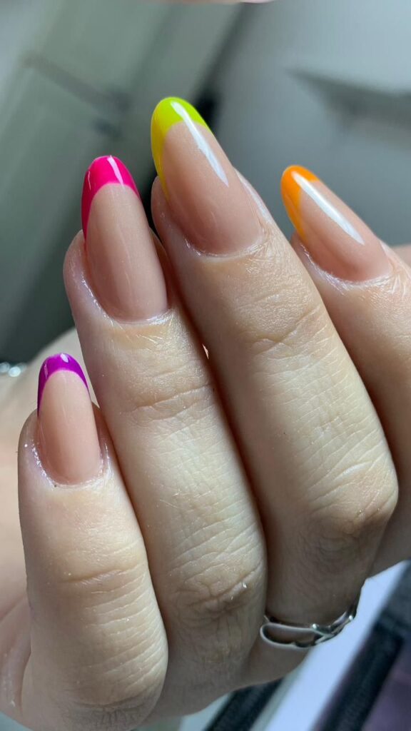 Unhas em formato amendoado com francesinha colorida em tons de neon, incluindo rosa, laranja e verde-limão.