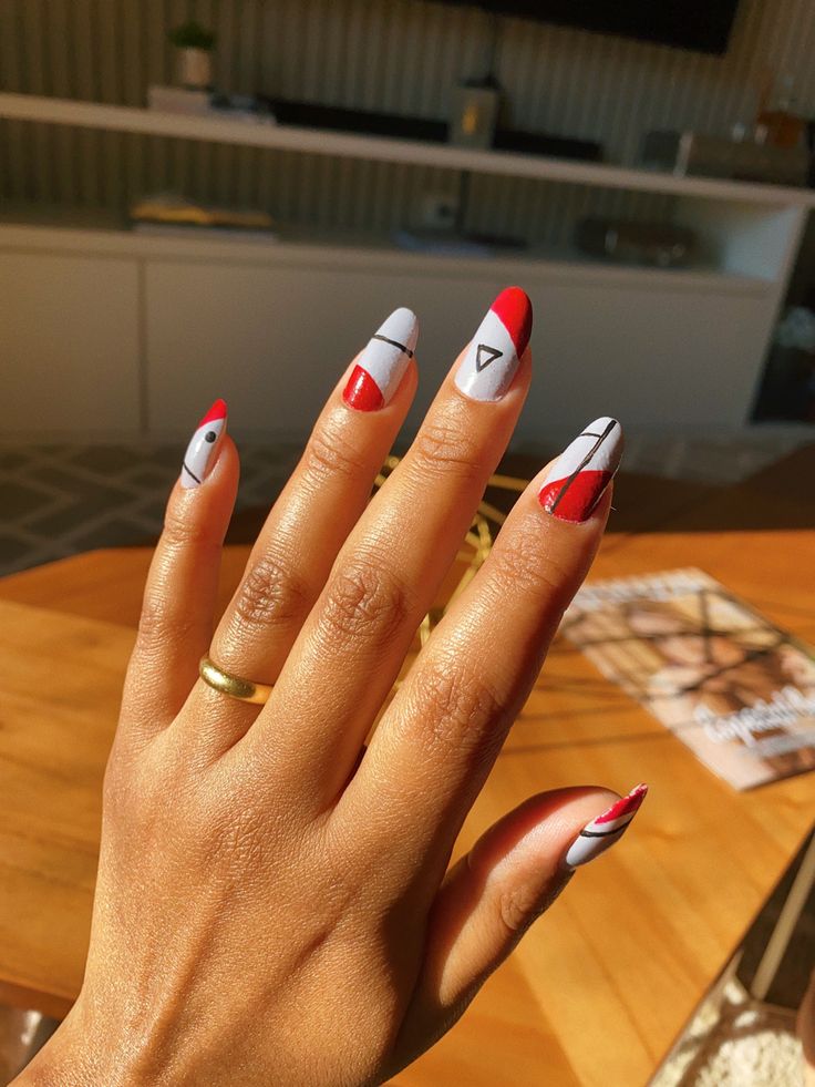 Unhas com um design geométrico moderno em tons de vermelho, cinza e preto.