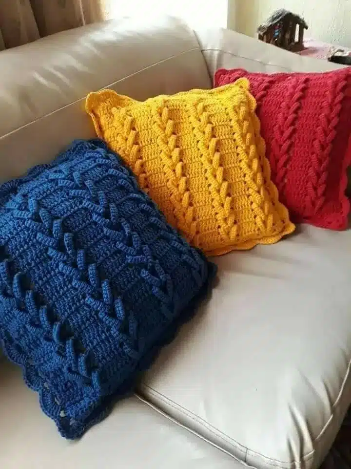 Almofadas de crochê 3D em cores vibrantes: azul, amarelo e vermelho, com padrão de trançado.