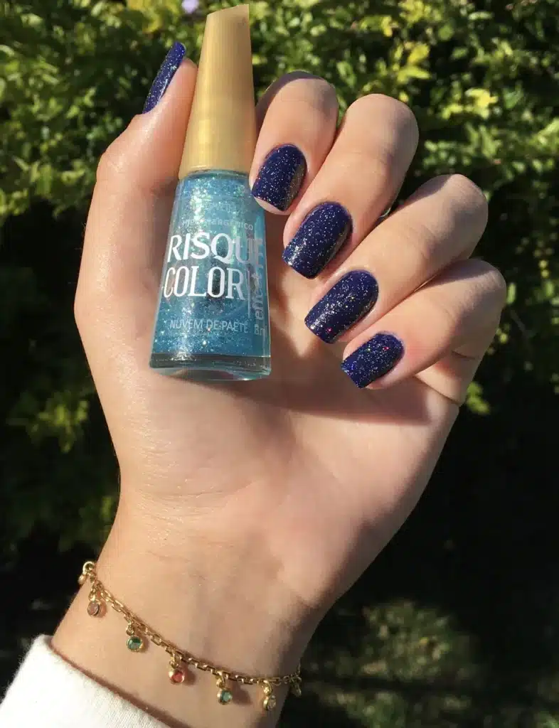 Unhas com esmalte azul escuro cintilante com glitter, destacando o brilho e o glamour da manicure.