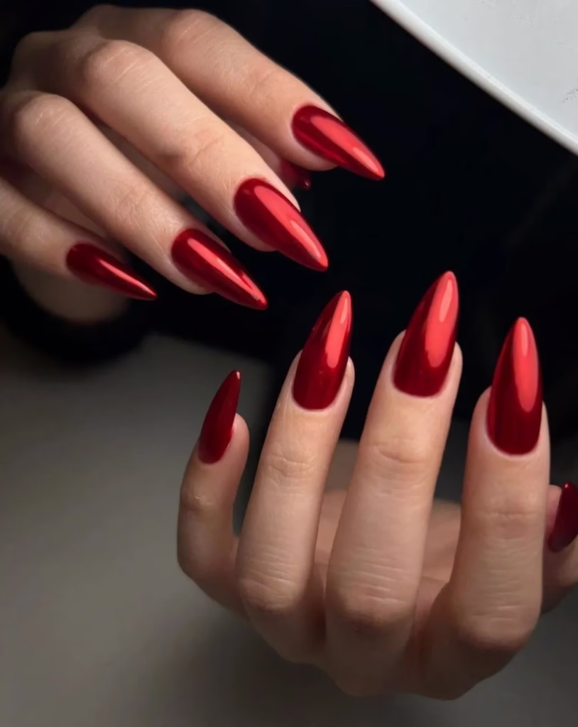 Unhas vermelhas com acabamento metálico e formato pontiagudo.