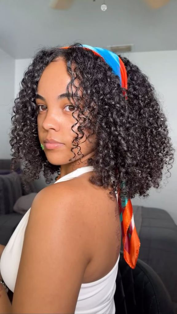 Mulher com cabelo cacheado usando lenço colorido como fita na cabeça