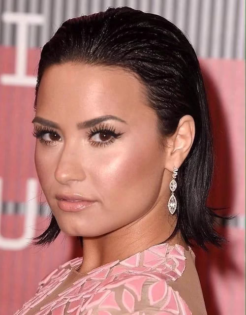 Demi Lovato com penteado molhado, cabelo para trás e brincos brilhantes