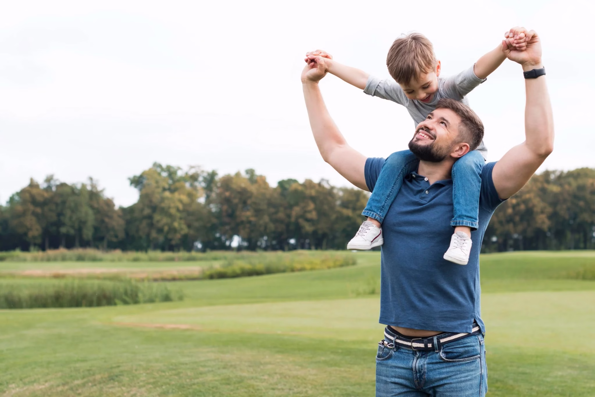Pai segurando seu filho nos ombros em um campo aberto, ambos sorrindo, representando momentos de afeto e diversão no Dia dos Pais.