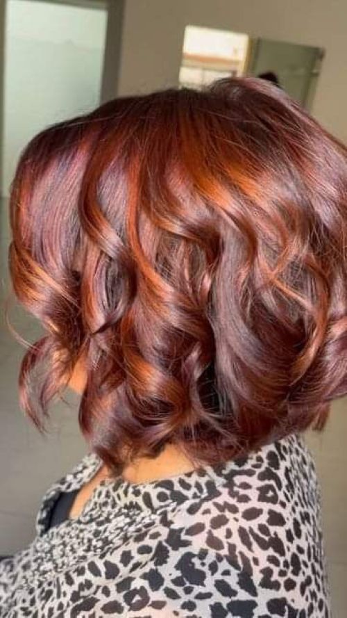 A visão traseira de uma mulher com cabelos na altura do ombro, com ondas soltas e mechas em tons de cobre avermelhado.