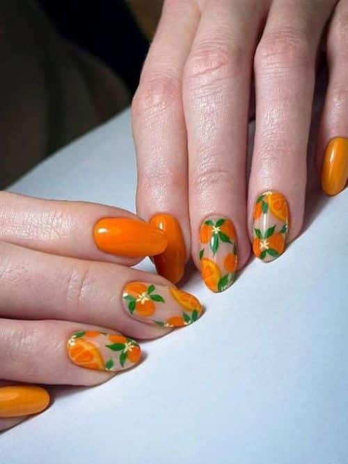 A imagem de uma mão com as unhas decoradas com nail art de tangerinas e flores.
