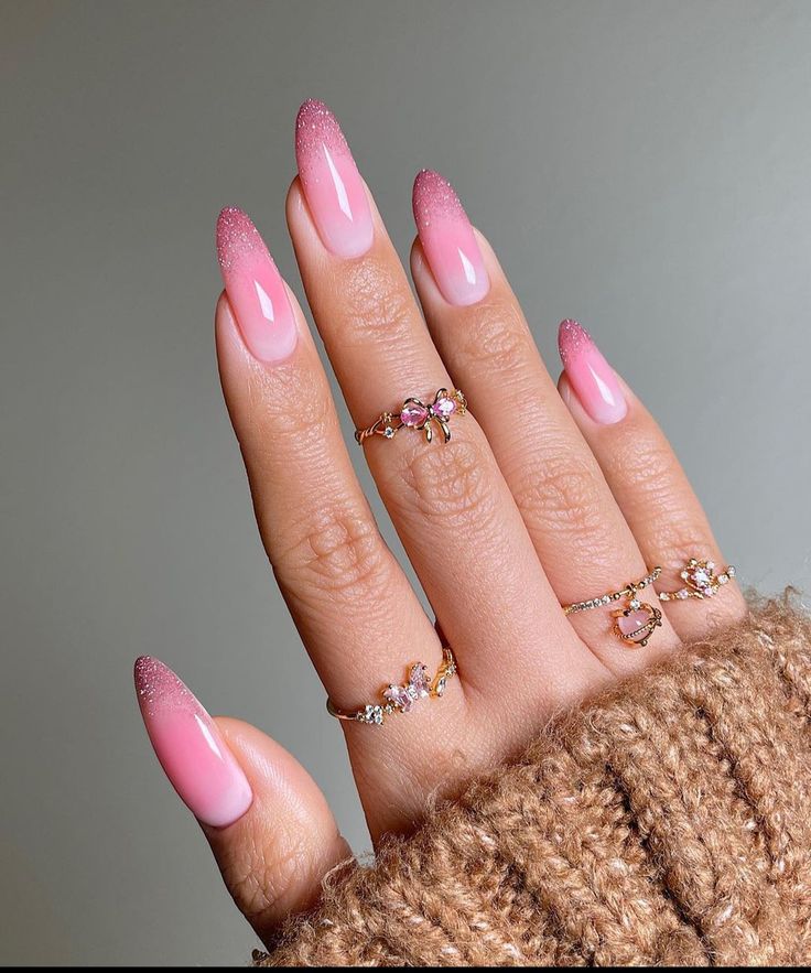 Mão com unhas longas, formato amendoado, com esmalte em degradê suave em tons de rosa e branco.