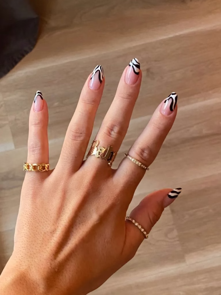 Unhas com francesinha preta e branca em estilo abstrato sobre base nude.