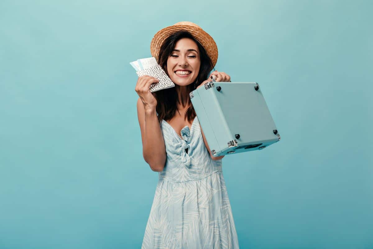 Mulher sorridente segurando ingressos e mala pequena, simbolizando viagem nos feriados prolongados de setembro