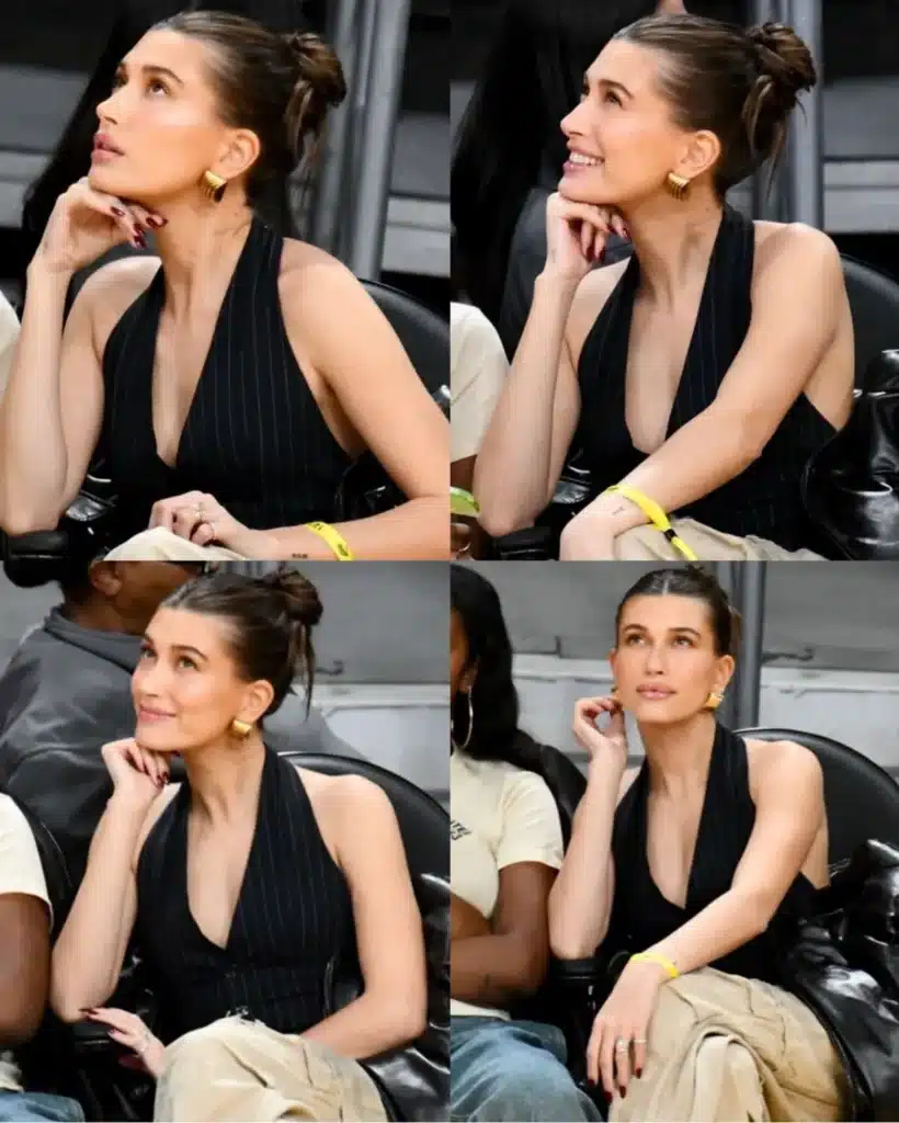 Hailey Bieber com cabelo sleek Hailey Bieber com cabelo sleek em evento, usando blusa preta e calça clara, observando atentamente.