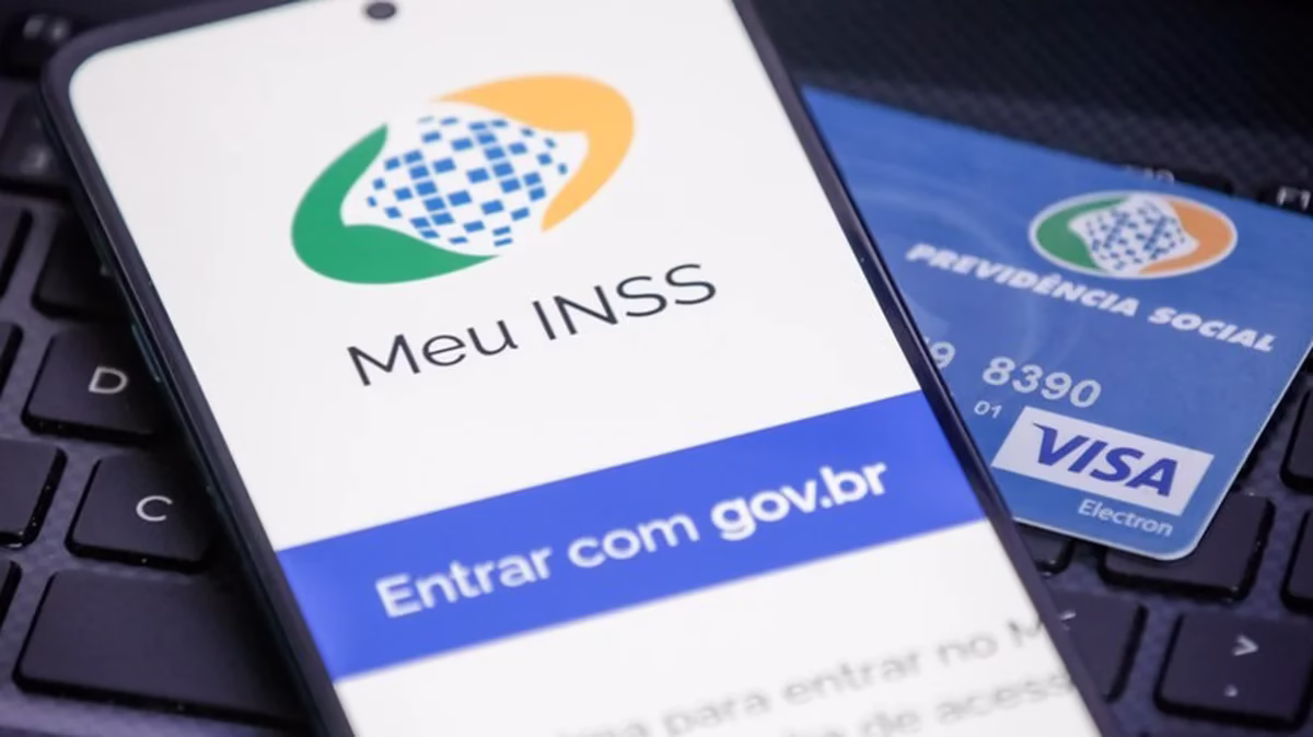 Logo do Meu INSS exibido em um smartphone com cartão de Previdência Social ao fundo.