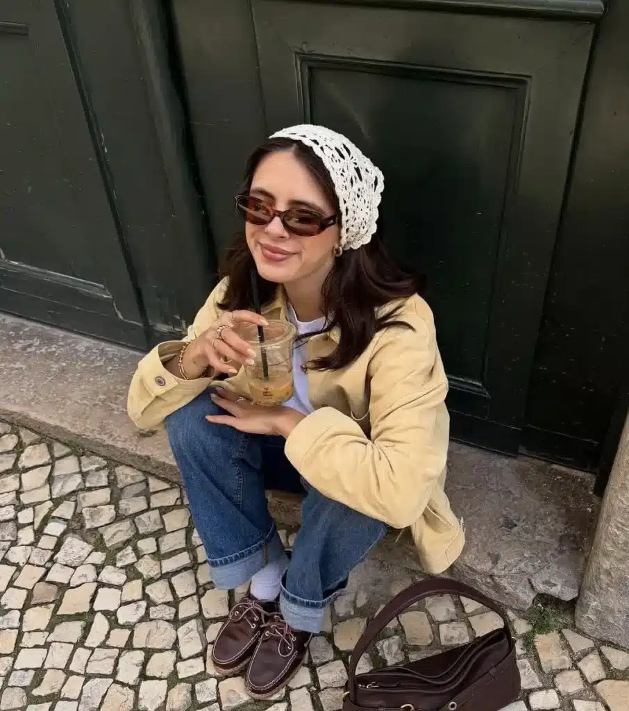Mulher sorrindo enquanto usa uma bandana de crochê e segurando uma bebida.