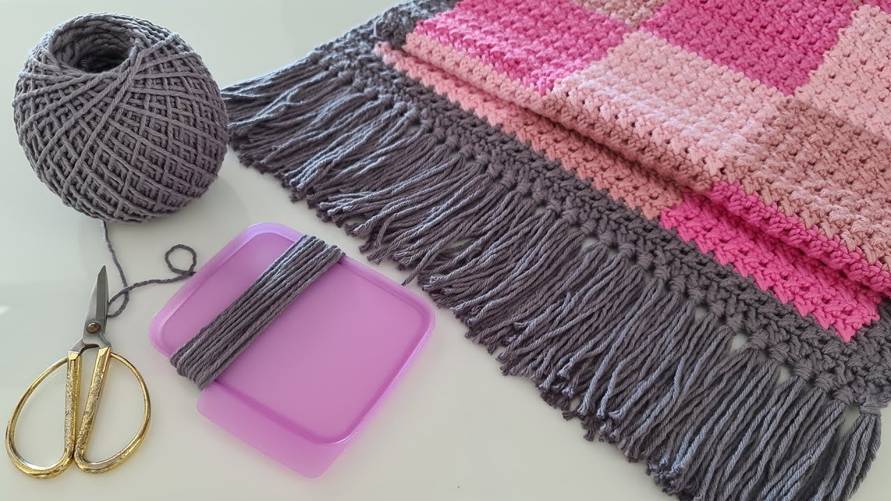 Acessórios e materiais para crochê, incluindo um novelo de lã cinza, tesoura e uma peça de crochê rosa, prontos para a confecção de um tapete.