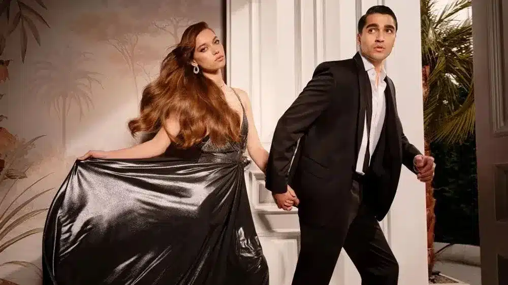 Cena dramática de O Canto do Pássaro com casal em pose elegante, representando o conflito e o romance da trama.