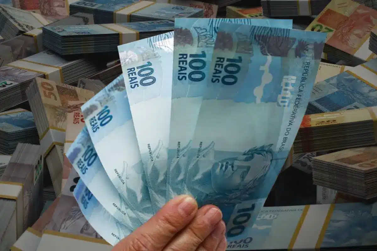 Pessoa segura notas de 100 reais, representando saque do Caixa Tem.