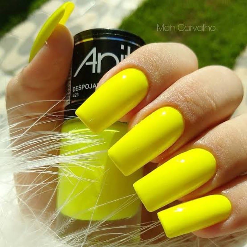 "Unhas com esmalte amarelo neon, destacando a cor vibrante em contraste com o fundo.