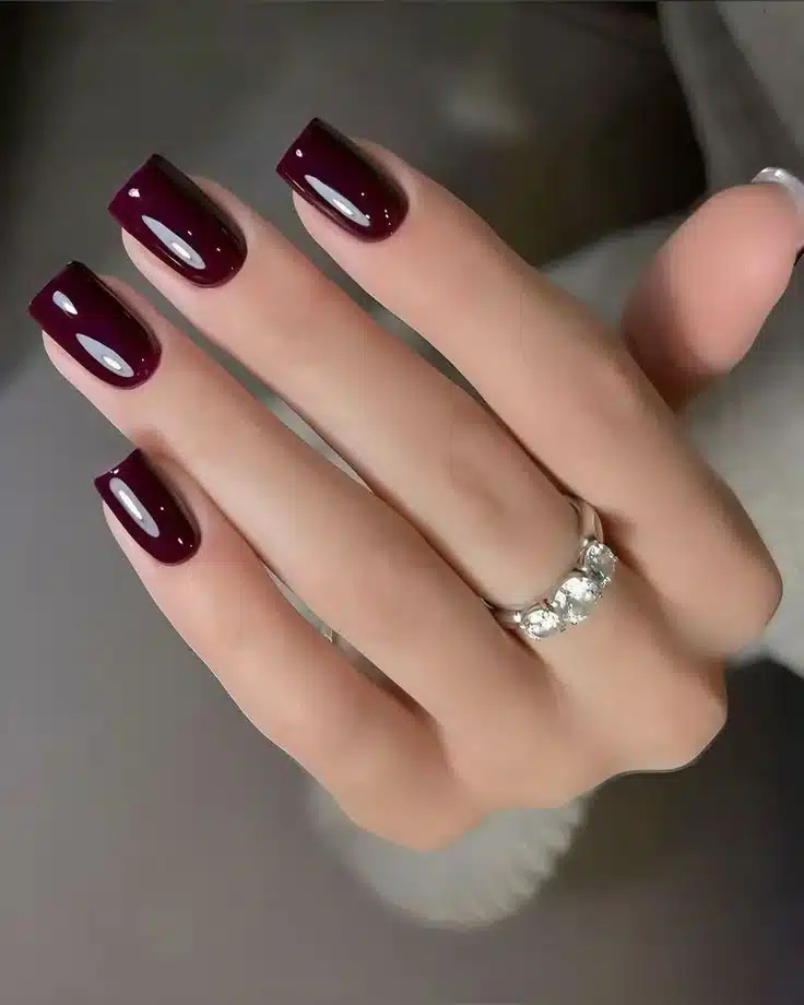 Unhas pintadas com esmalte vinho escuro glossy, destacando o brilho e acabamento elegante.