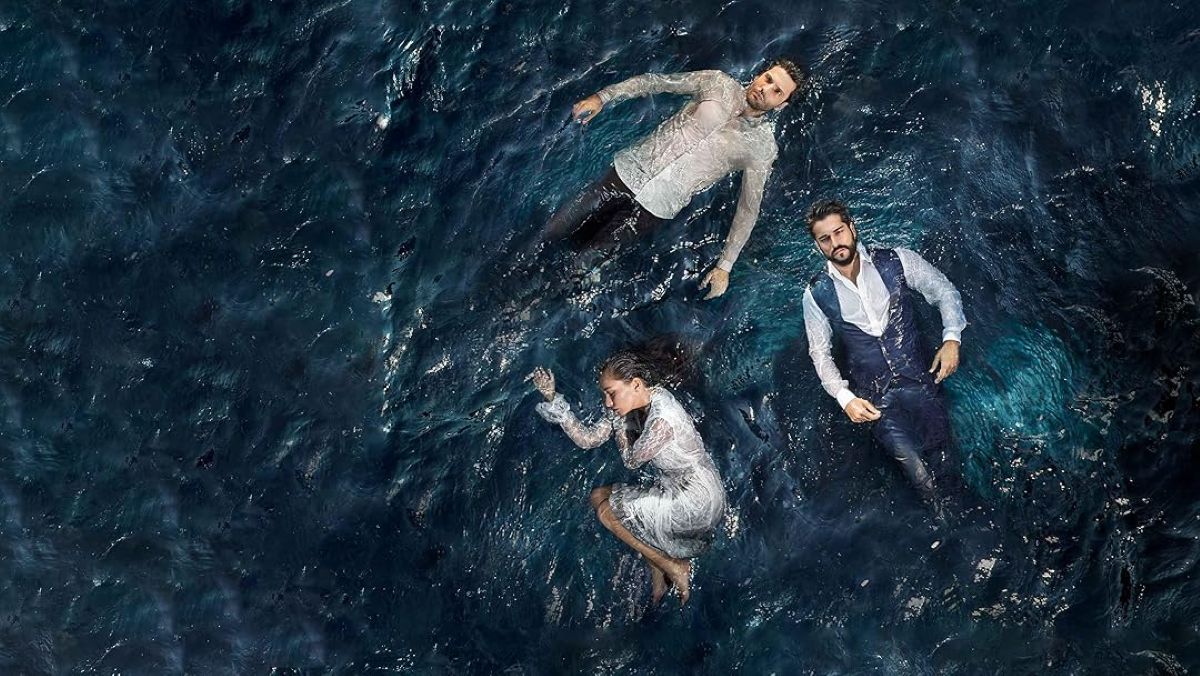 Três atores de novela turca flutuando em águas escuras. Os homens vestem camisas sociais e a mulher, um vestido branco.