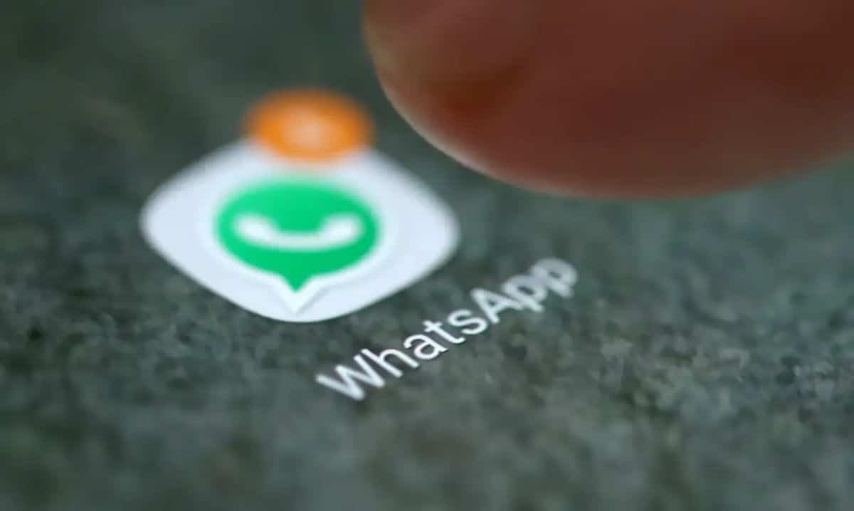 Um dedo tocando o ícone do aplicativo WhatsApp em uma tela de celular, com o nome do aplicativo visível, representando as interações do usuário com o app e seus possíveis riscos de segurança.