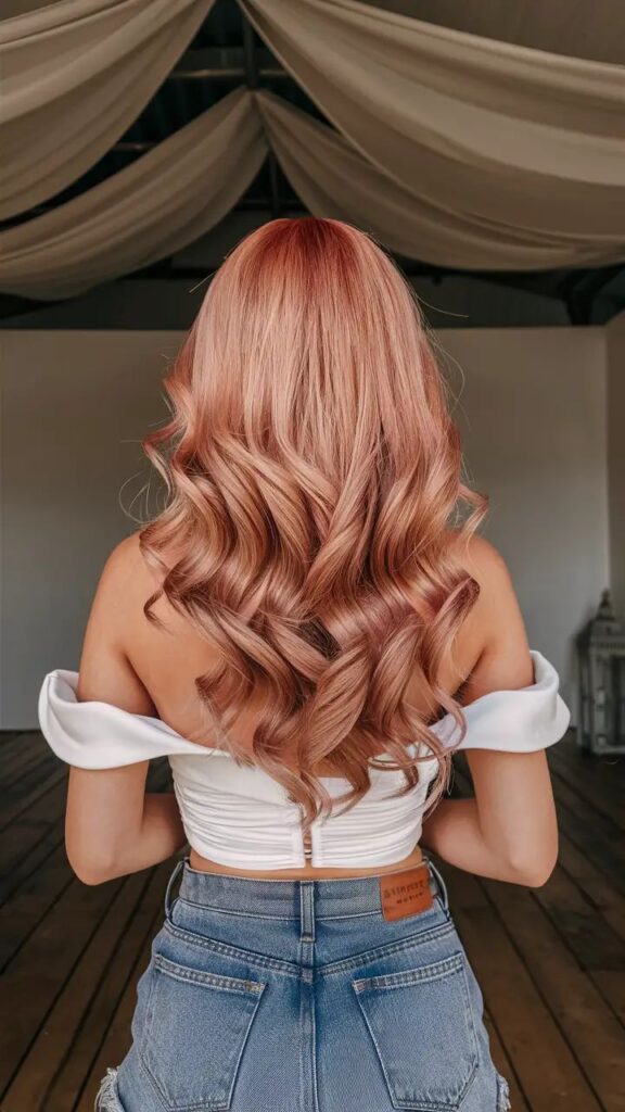 Mulher de costas com longos cabelos ondulados na cor strawberry blonde, exemplificando a tendência de ruivo claro.