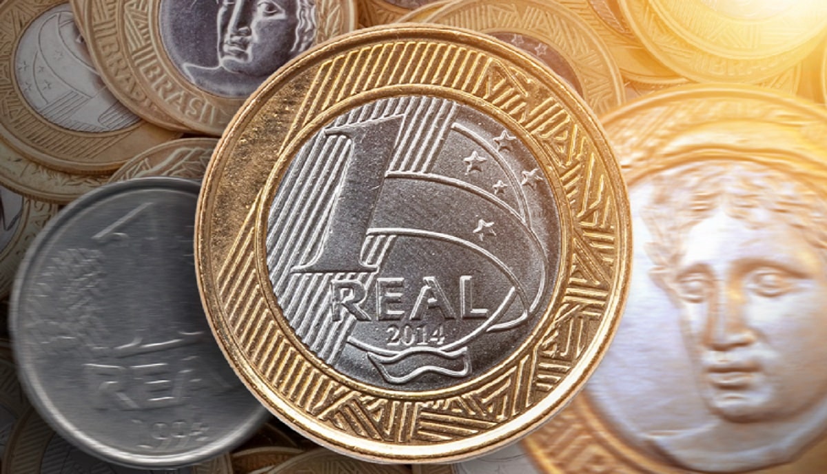 Close em uma moeda de 1 real brasileira com detalhes da bandeira e estrelas, rodeada de outras moedas