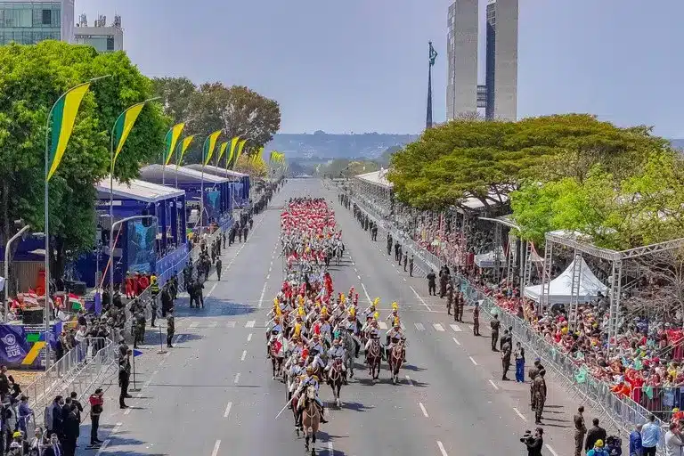 Desfile de 7 de setembro em 2024, com cavaleiros e grupos de pessoas marchando em uma avenida decorada para o evento.